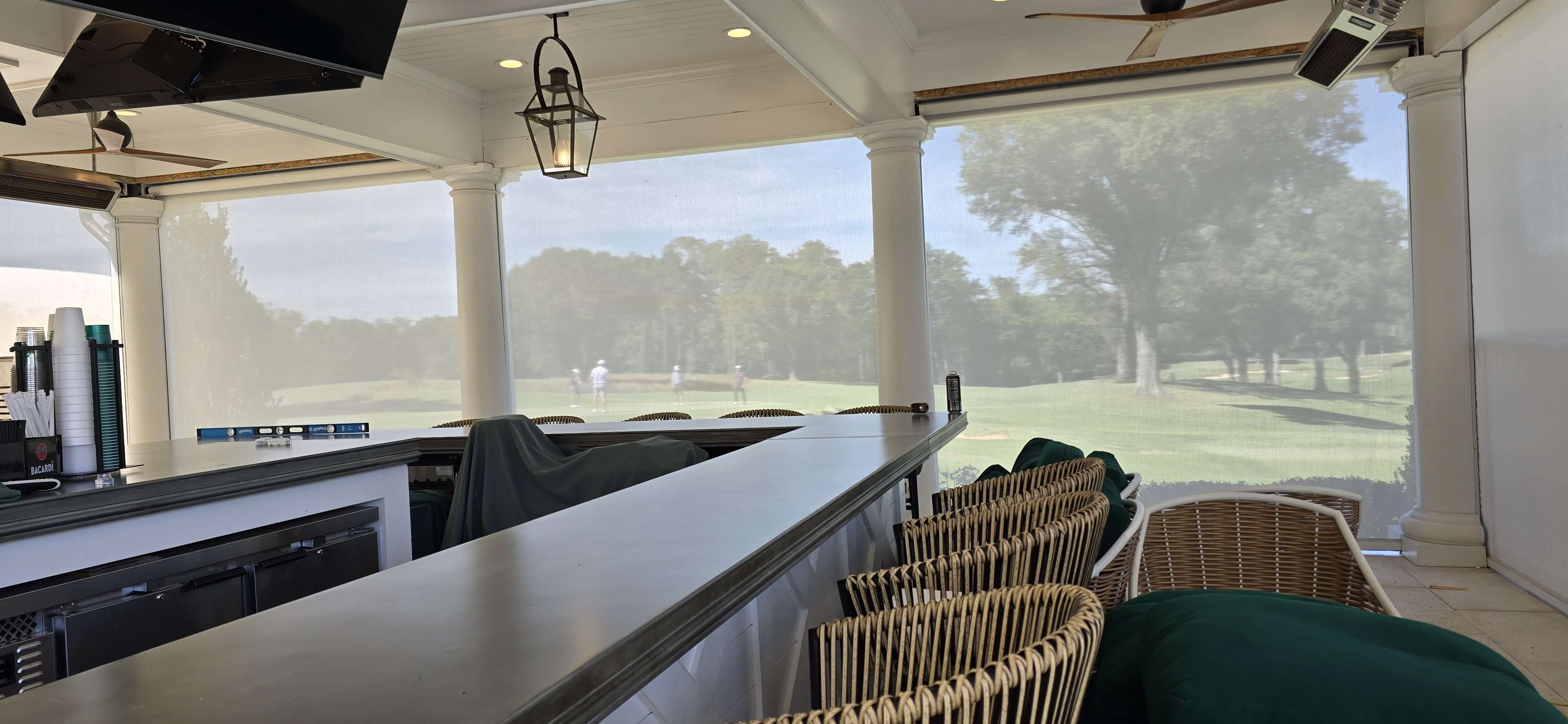 Motorized screen shades lowered over a clubhouse bar overlooking the golf course